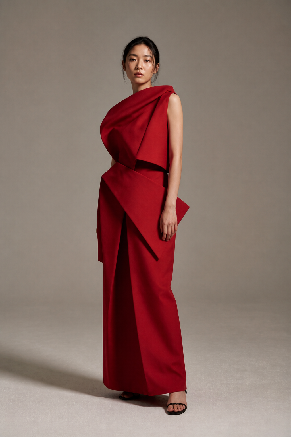 Model in a sculptural red garment photographed in a warm gray studio